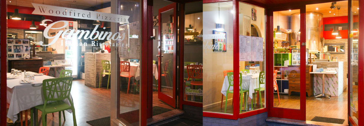 Front dining room at Gambinos with colourful chairs, red-accented decor and the wood-fired oven.